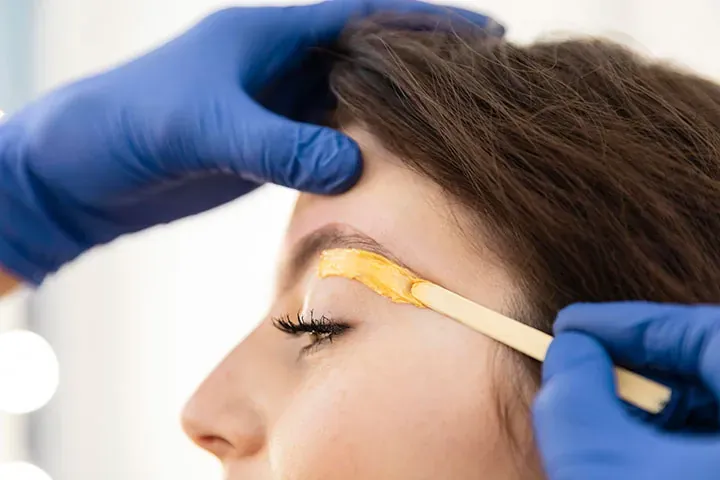 Esthetician shaping a client's eyebrow with warm sugar wax