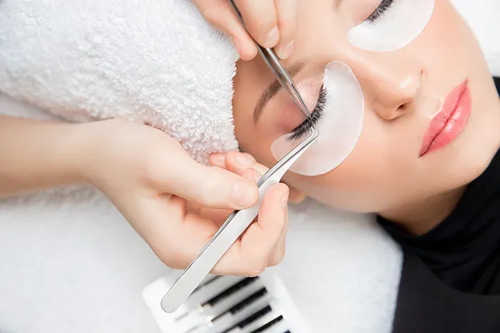 Esthetician applying a single classic eyelash extension with tweezers to a client's eye